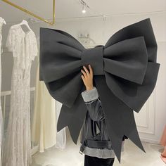 a person is holding up a giant bow in front of dresses on mannequins