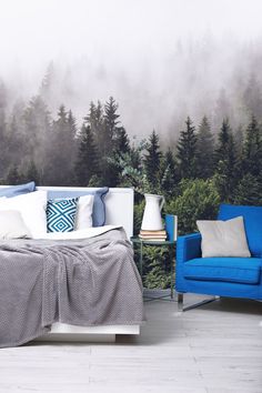 a bed sitting next to a blue chair in front of a forest wallpapered with trees