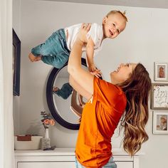 a woman holding a baby up in the air while standing next to a dryer