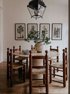 a dining room table with chairs and pictures on the wall above it, along with two vases filled with flowers