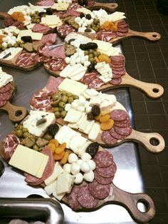 an assortment of meats, cheese and olives on a metal tray with wooden spoons