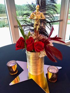 a gold vase with roses in it sitting on a star shaped table next to two shot glasses