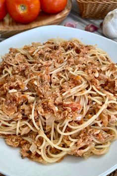 a white plate topped with pasta covered in meat and sauce next to some fresh tomatoes