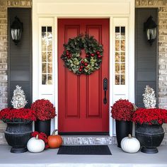 a red front door with two black planters and a wreath