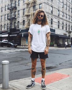 a man with long hair and tattoos standing on the sidewalk