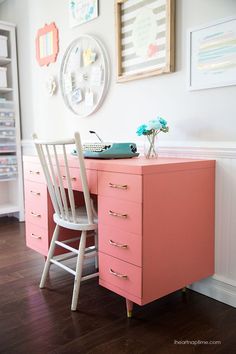 a pink desk and chair in a room with pictures on the wall behind it,