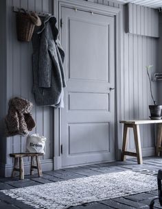 a teddy bear sitting on a stool in front of a white door with two coats hanging from it's hooks