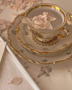 a fancy cup and saucer on a marble counter top with rose petals scattered around it