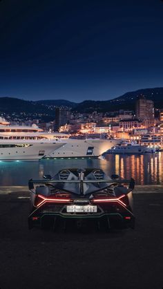 a sports car parked in front of a cruise ship at night with the lights on