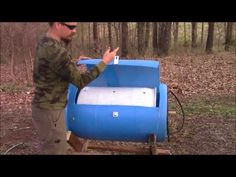 a man standing next to a blue barrel in the woods