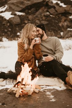 a man and woman sitting next to a campfire drinking coffee