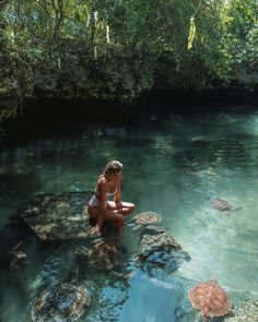 a woman sitting on rocks in the middle of a river with turtles swimming around her