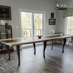 a dining room table in the middle of a living room with hardwood floors and large windows