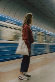 a woman is waiting for the train to arrive at the station and she's holding a bag