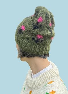 a woman wearing a green knitted hat with pink flowers on the top and bottom