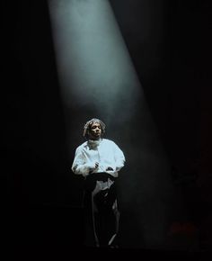 a man in white shirt and black pants standing on stage with his arms folded out