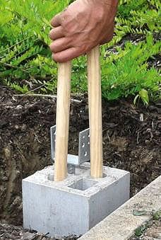 a hand holding two wooden mallets over a cement block in front of some bushes