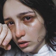 a close up of a person wearing a white shirt and holding their hand to her face