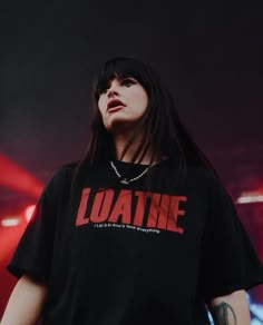 a woman with long black hair standing in front of a red and white sign that says loathe