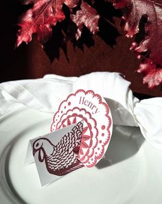 a white plate topped with a turkey cut out of paper next to a red leaf