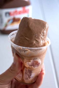 a hand holding an ice cream sundae in a plastic cup with chocolate frosting on top