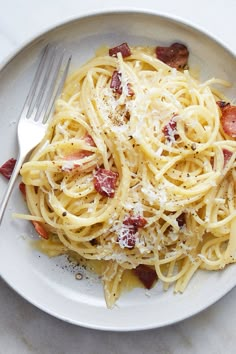 a plate of spaghetti with bacon and parmesan cheese on it, ready to be eaten