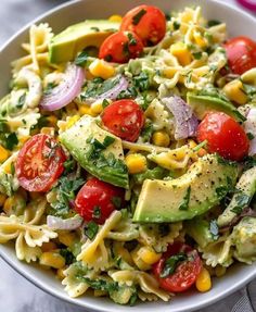 a white bowl filled with pasta salad topped with avocado, tomatoes and corn