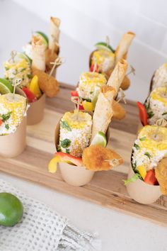 several appetizers are arranged in small cups on a cutting board with limes