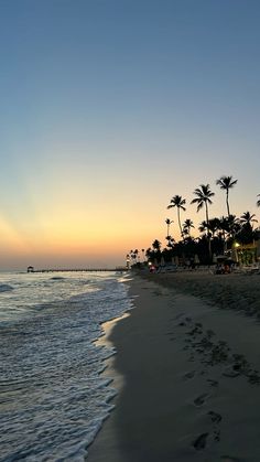 a beach with palm trees and the sun setting in the sky over the water at dusk