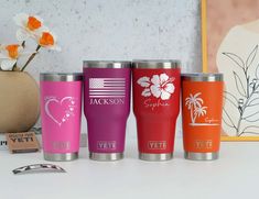 three different colored tumblers sitting on top of a table next to a vase with flowers