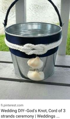 a bucket with a rope and seashell hanging from it on a porch next to water