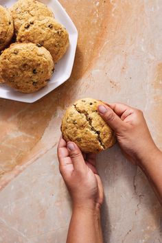 a person holding a cookie in their hand next to some cookies on a white plate