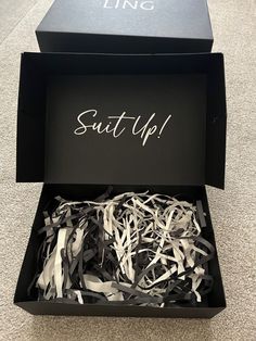 an open black box with white ribbons in it that says suite up on the inside