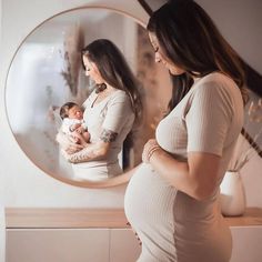 a pregnant woman standing in front of a mirror with her baby girl looking at herself