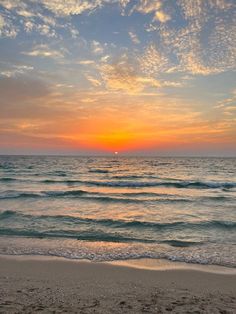 the sun is setting over the ocean with waves coming in to shore and sand on the beach