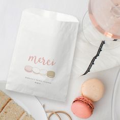 a white paper bag with macaroons on it next to some bread and wine glasses