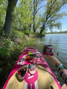 a person is holding up a cup while sitting on a boat in the water near some trees