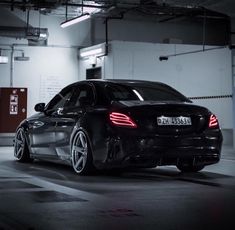 the rear end of a black car parked in a parking garage with its lights on