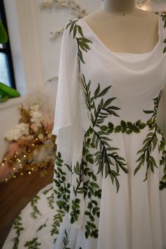 a white dress with green leaves on it and a mannequin in the background