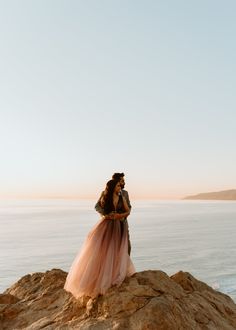 a man and woman standing on top of a rock next to the ocean with their arms around each other