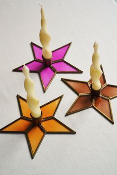 three candles are sitting in the shape of stars on a white tablecloth with purple and orange colors