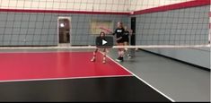 two women are playing volleyball in a gym with red and gray walls, while one woman is about to hit the ball