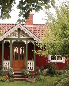 a small red and white house with flowers in the front yard