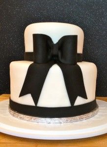 a white and black cake with a big bow on it's top, sitting on a table