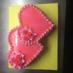 two heart shaped cakes with pink frosting and roses on top are sitting on a yellow plate