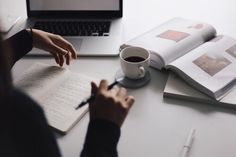 a person sitting at a desk writing in front of a laptop computer and coffee cup