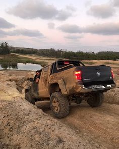 a black truck driving down a dirt road next to a body of water with trees in the background