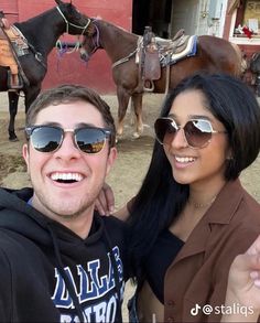 a man and woman taking a selfie with horses in the back ground behind them