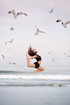 a woman jumping in the air with seagulls flying above her and on the beach