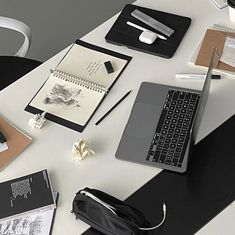 a laptop computer sitting on top of a white desk next to a notebook and pen